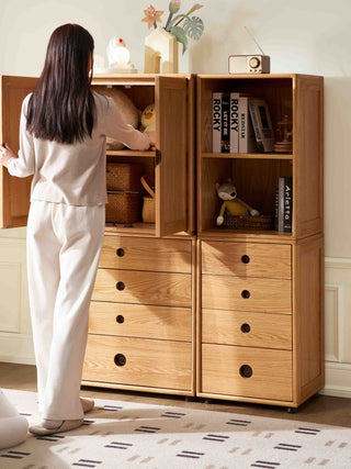 Person organizing a wooden cabinet with books and decorative items.