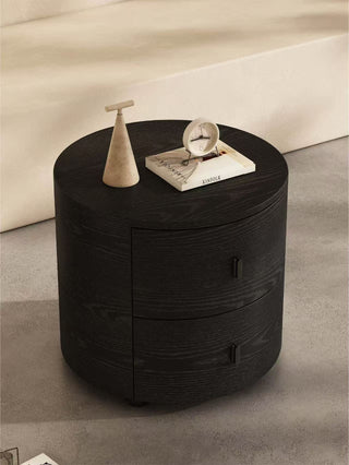 Round black nightstand with decorative items on a neutral background