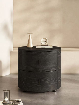 Round nightstand table with decorative items against a beige wall.