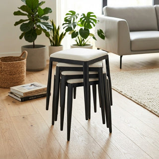 Stack of black stools with white cushions in a living room setting with plants and books.