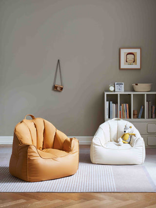 Two bean bags, one yellow and one white with a dog plush toy, in a room with a bookshelf and decorative items.