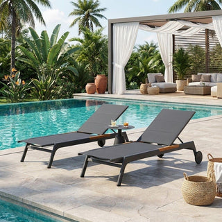Two gray lounge chairs by a pool with palm trees and a cabana in the background.
