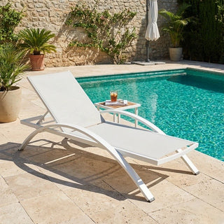 White lounge chair by a pool with a drink on a small table