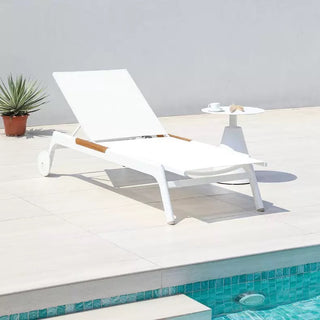 White lounge chair by a pool with a small table and plant