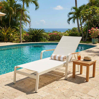 White lounge chair with a striped towel and a small table by a poolside with palm trees and ocean view.