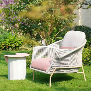 White wicker chair with pink cushions on a grassy area with greenery in the background