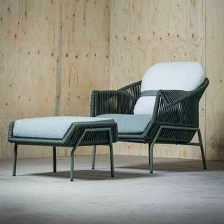 Wicker chair and ottoman set with white cushions against a wooden wall.