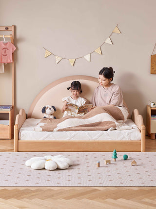 Woman and child reading on a wooden bed in a cozy room with toys and decorations.