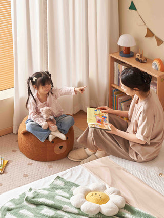 Woman and child sitting on the floor in a cozy room, with the woman reading a book to the child.
