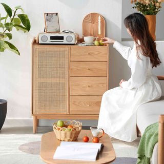 Woman sitting on a couch in a living room with a wooden cabinet and decorative items.