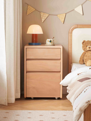 Wooden bedside table with lamp and decorative items next to a bed with a teddy bear and pillows.