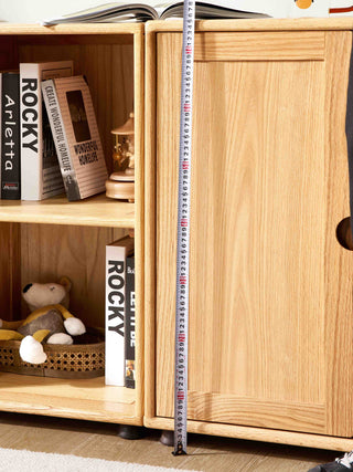 Wooden cabinet with books and a teddy bear, tape measure for scale.