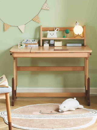 Wooden desk with shelves against a green wall, decorated with small items and a lamp.