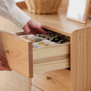 Wooden drawer being opened to reveal neatly folded clothes inside.