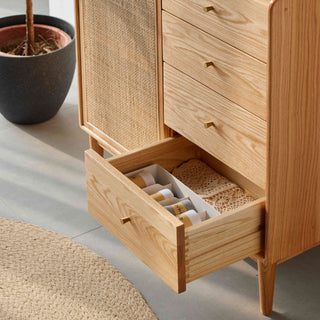 Wooden dresser with open drawer containing bottles, on a light wooden floor.