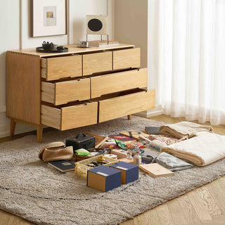 Wooden dresser with open drawers in a room with a rug and various items on the floor.
