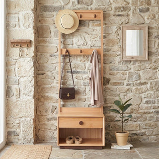 Wooden hall tree with coat hooks, drawer, and shoe storage against a stone wall.