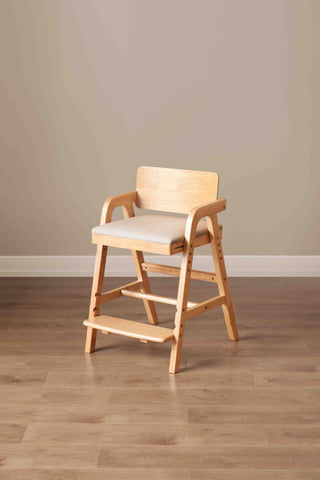 Wooden high kids chair with a cushion on a wooden floor against a beige wall