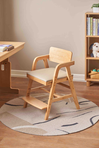 Wooden kids chair with cushion on a round rug in a room with a desk and bookshelf.