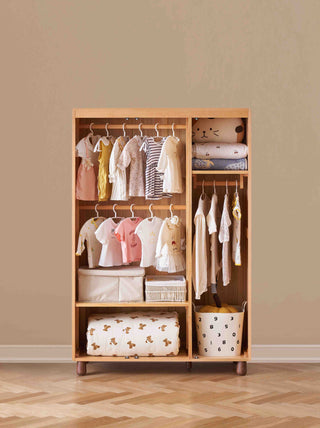 Wooden kids wardrobe with clothes and storage baskets against a beige wall.