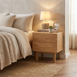 Wooden nightstand with lamp and decor next to a bed in a bedroom setting