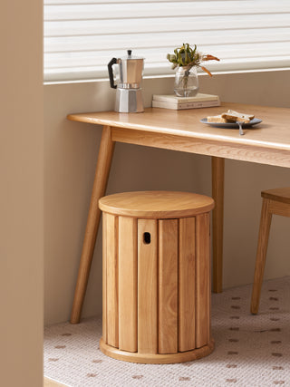 Wooden stool in front of a wooden table with a coffee maker and books on it.