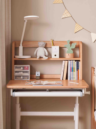 Wooden study desk with shelves, lamp, books, and decorative items against a beige wall.