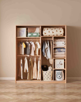 Wooden wardrobe with clothes and baby items against a beige wall.