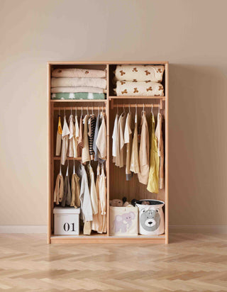 Wooden wardrobe with clothes and storage bins against a beige wall.
