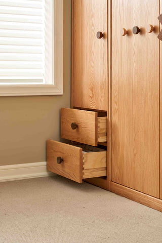 Wooden wardrobe with open drawers in a room with a window and beige walls.