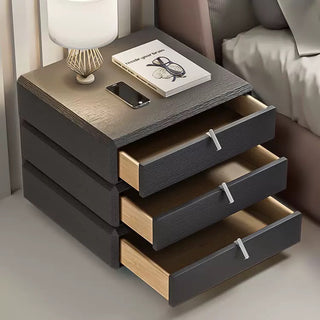 black nightstand with three drawers, a lamp, and a book on a neutral background.