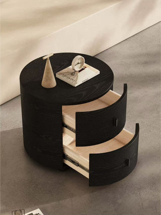 black round bedside table with a drawer on a gray floor.