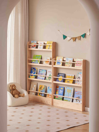 childrens wooden bookshelf with children's books in a room with a teddy bear and decorative banner.
