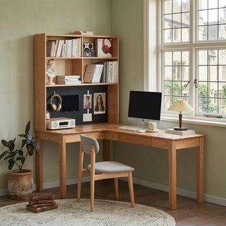 corner study table with bookshelf, chair, and computer setup in a room with large windows.