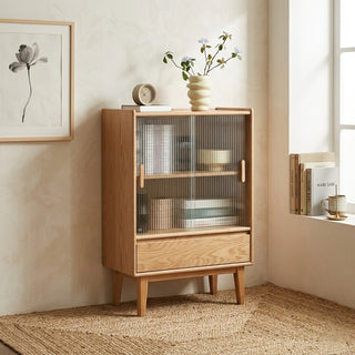 fluted glass cabinet with glass doors and a drawer in a room with a plant and books on top.