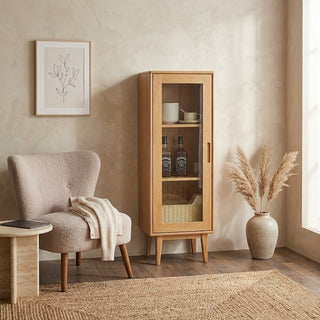 glass display cabinet, chair with blanket, and vase with dried plants in a room.
