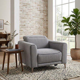 grey armchair in a living room with a brick wall and large window.