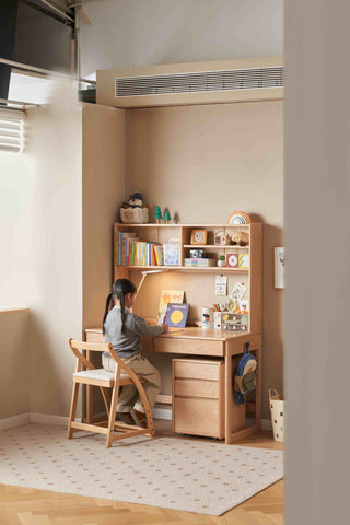kids sitting at a wooden desk in a small room with shelves and decor.