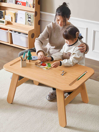 mother and child playing with toys at a childrens activity table in a room with shelves and a rug.