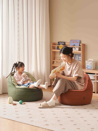 mother and child sitting on bean bags in a room with a bookshelf and toys.