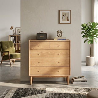 oak chest of drawer in a room with decor elements like books and a plant.
