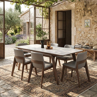 sintered stone dining table set outdoors with chairs on a stone patio in front of a stone building.
