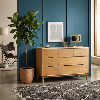 solid wood chest of drawers against a blue wall with a plant and decor items in a room.