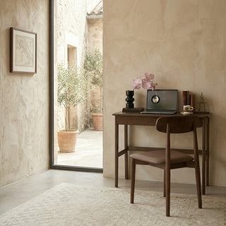 walnut study table with chair in a room with a large window showing an outdoor patio.